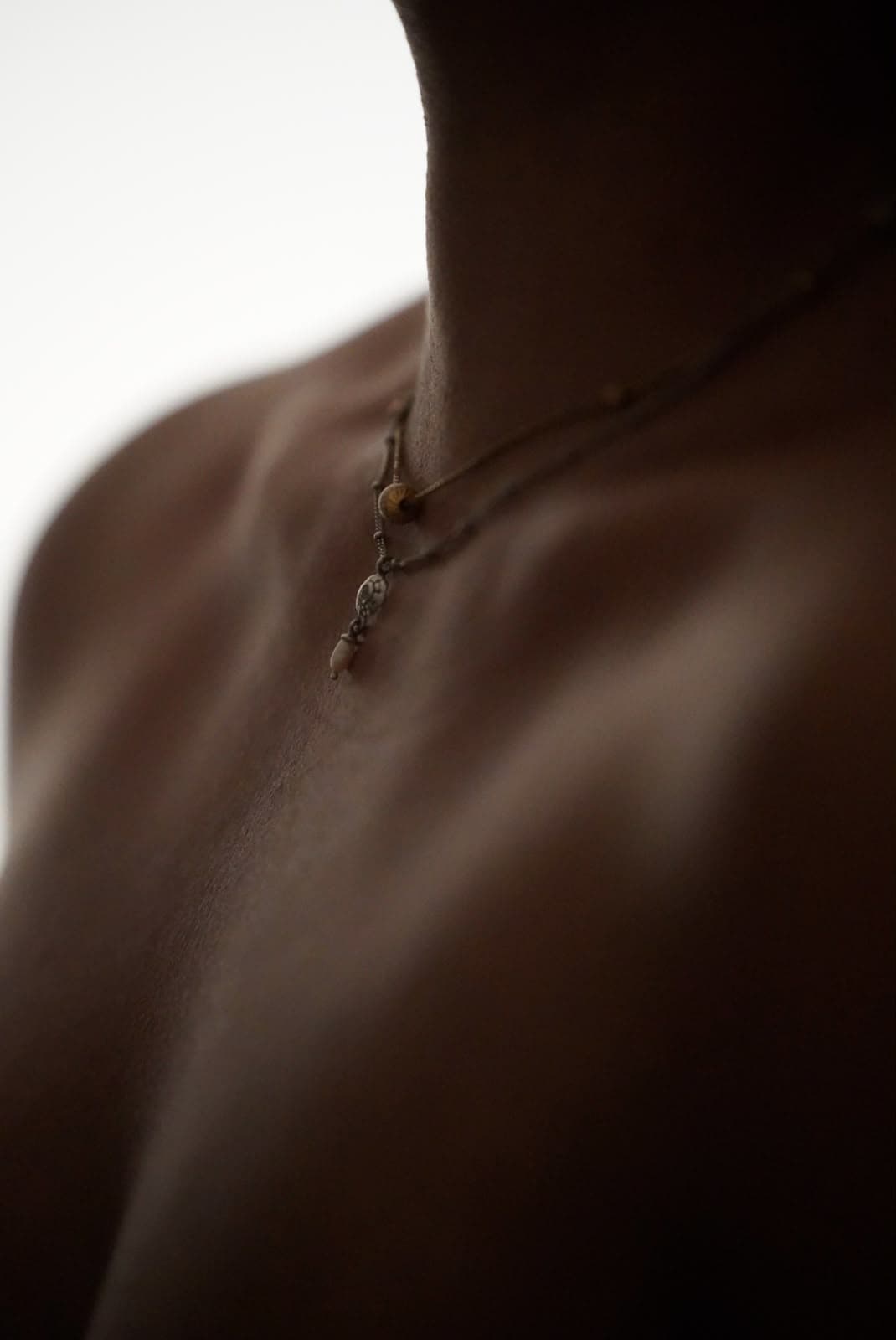 Close-up of a person's neck and collarbone featuring two delicate, layered necklaces in soft lighting.